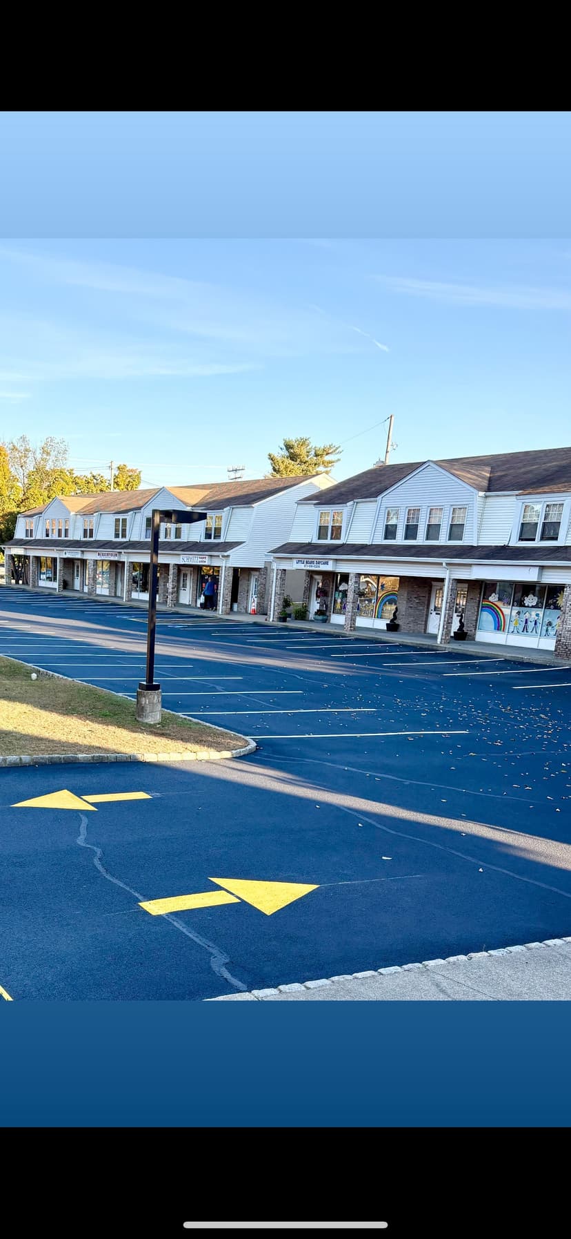 Row of storefronts along a blue-painted parking lot under clear blue sky.