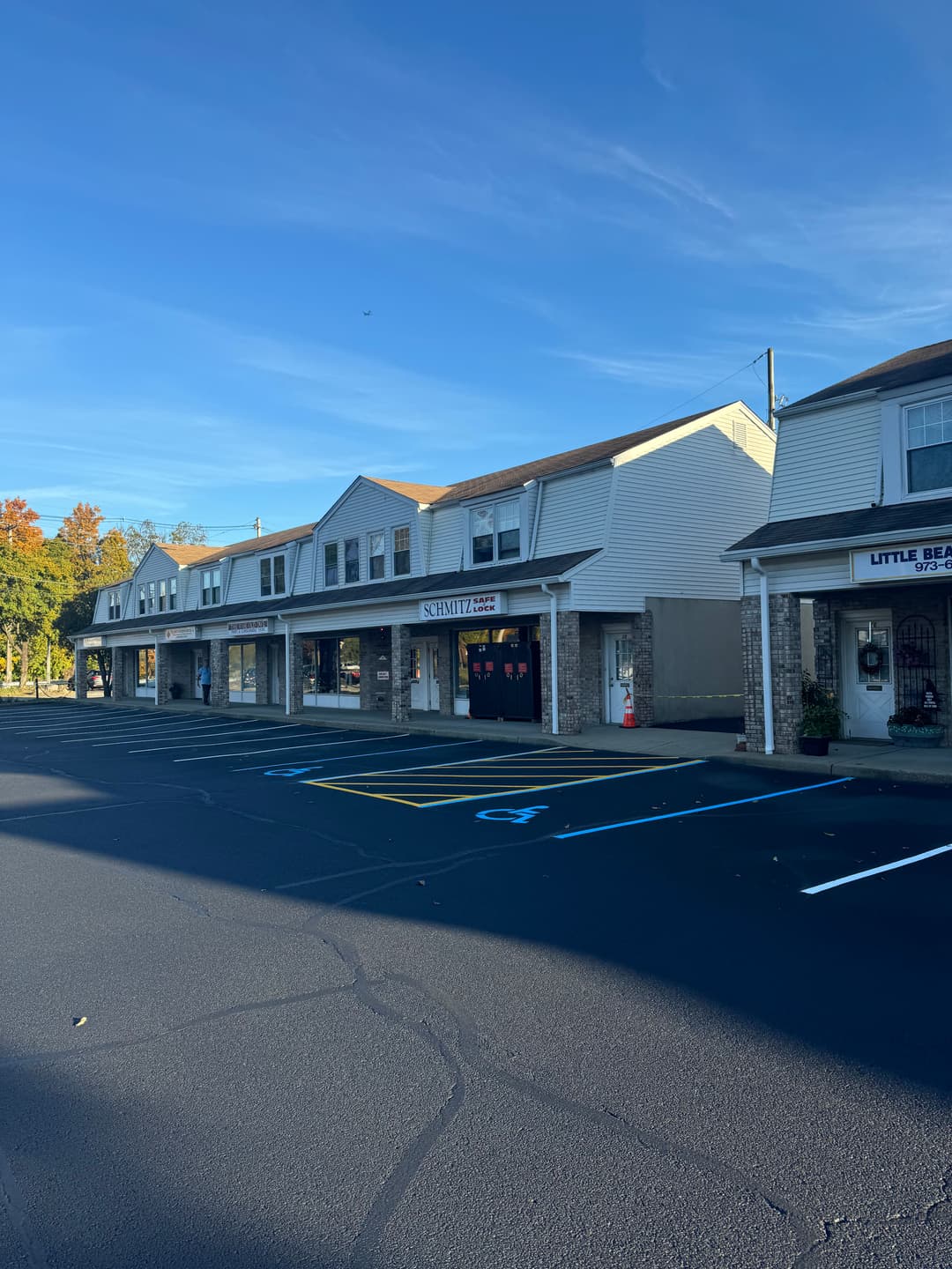 Exterior view of a retail plaza with parking lot and blue sky, featuring storefronts and signage.