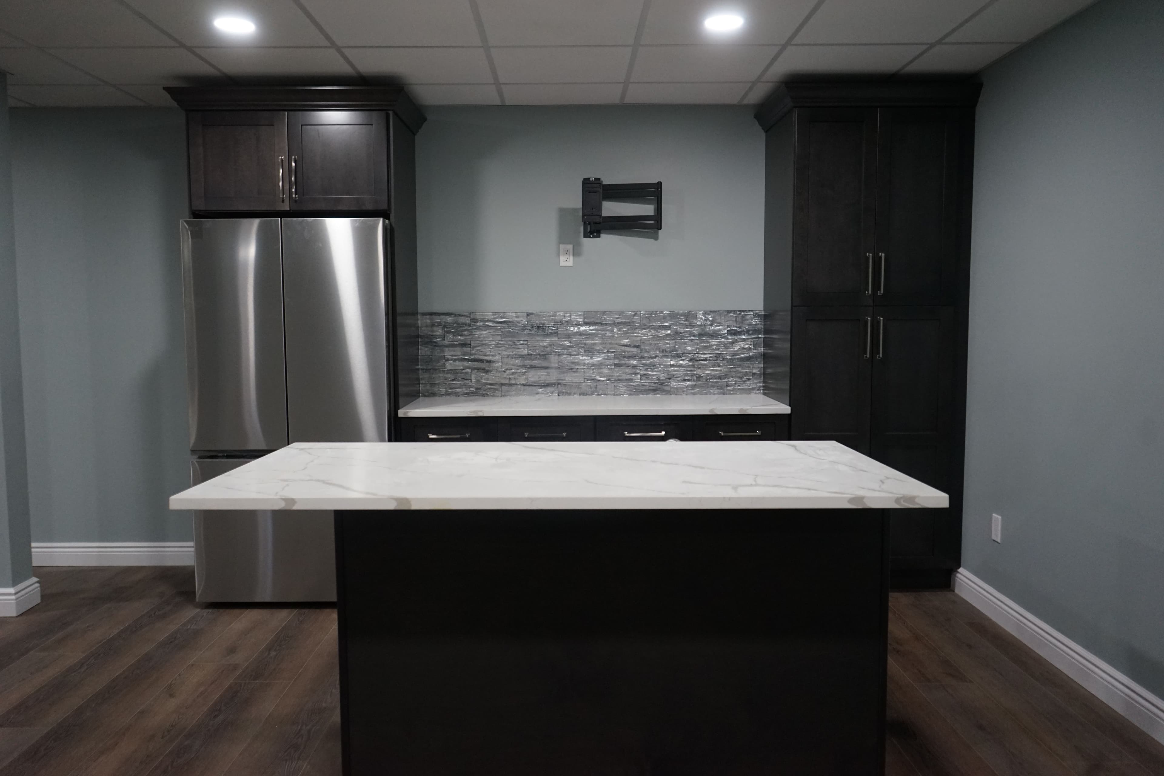 Modern kitchen with dark cabinetry, stainless steel fridge, and marble island countertop.