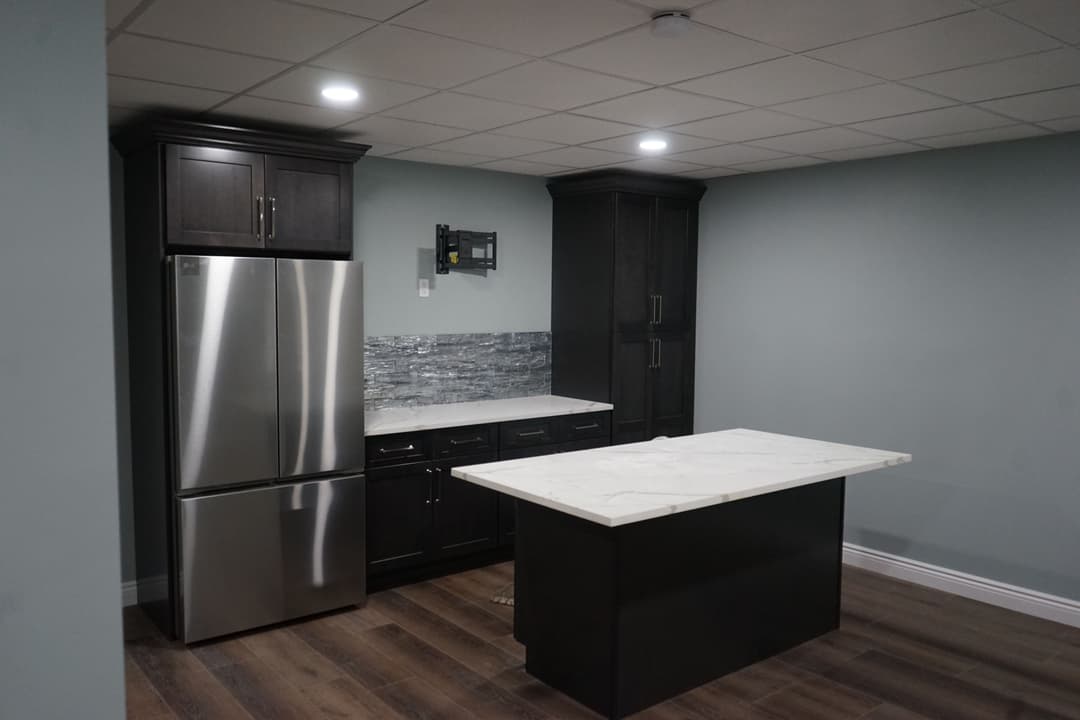 Modern kitchen with dark cabinetry, stainless steel fridge, marble island, and LED lighting.