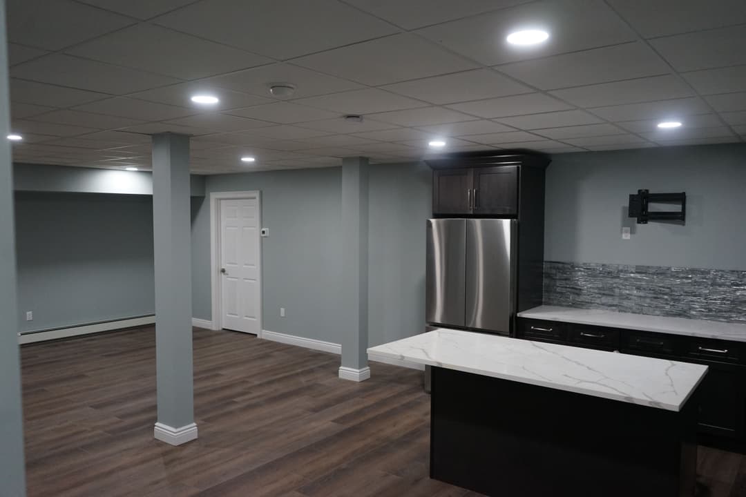 Modern basement kitchen with stainless steel appliances, island, and built-in lighting.