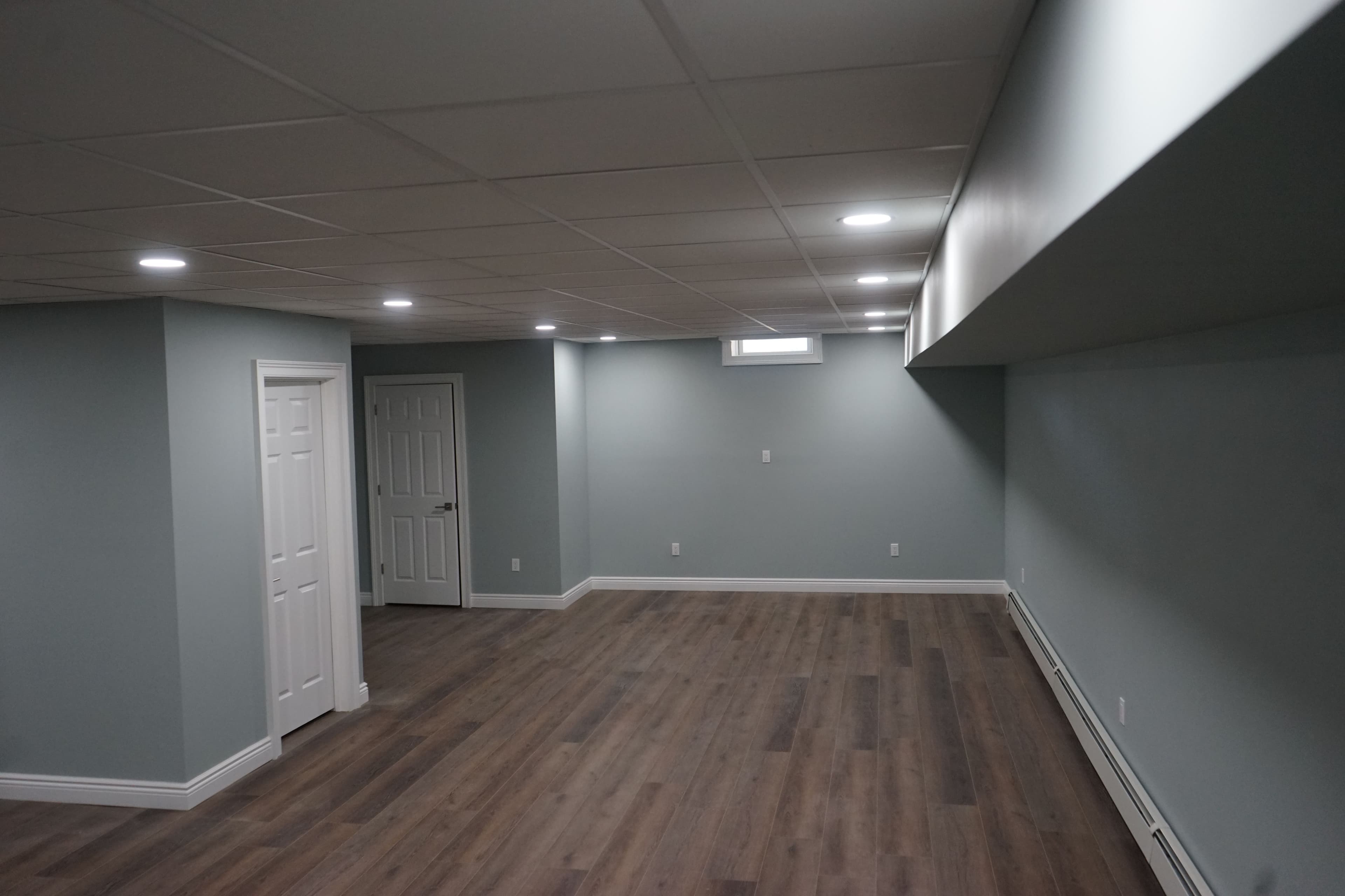 Spacious basement interior with light gray walls, wood flooring, and bright LED lighting.