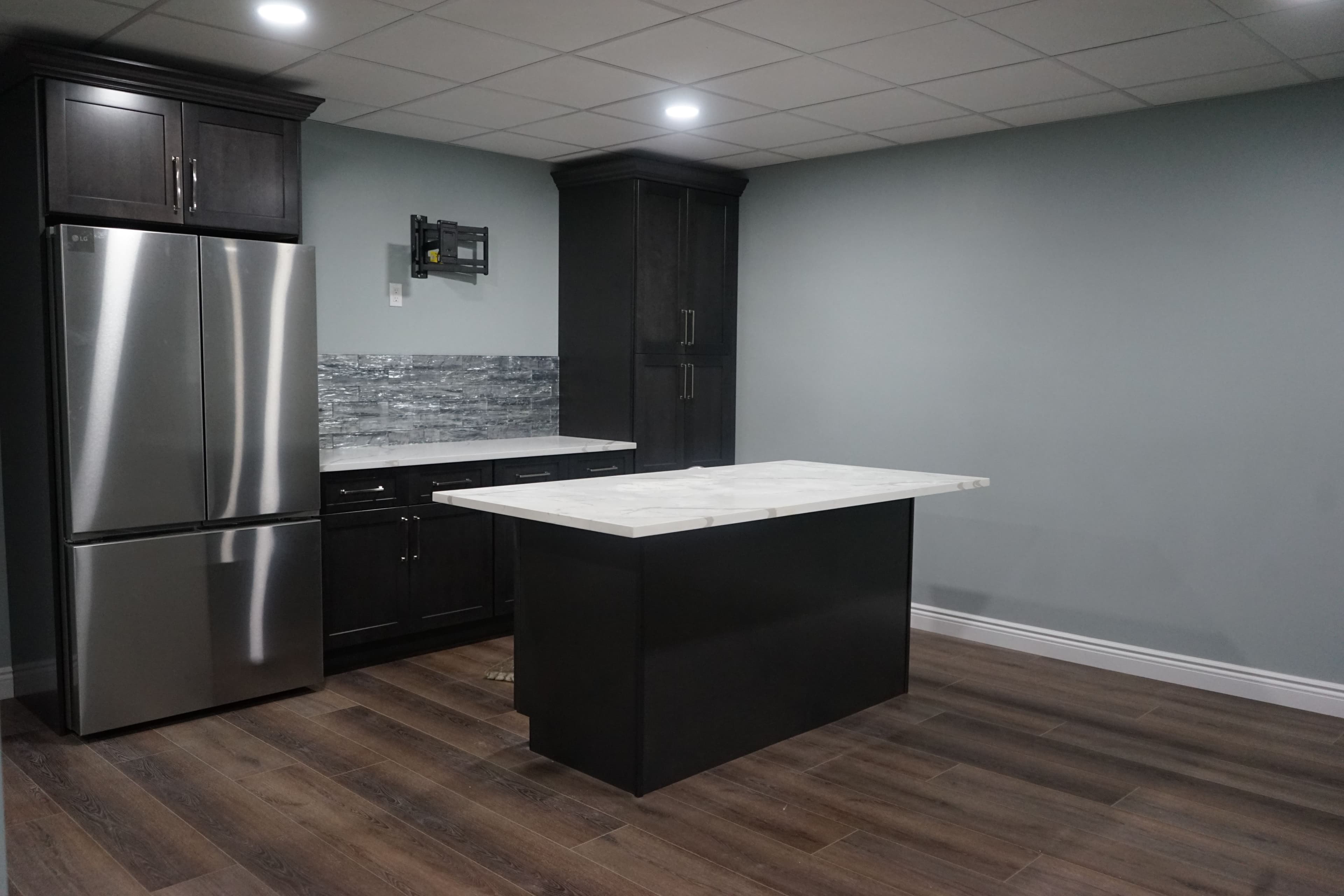 Modern kitchen with stainless steel appliances and marble island, featuring dark cabinetry and wood flooring.