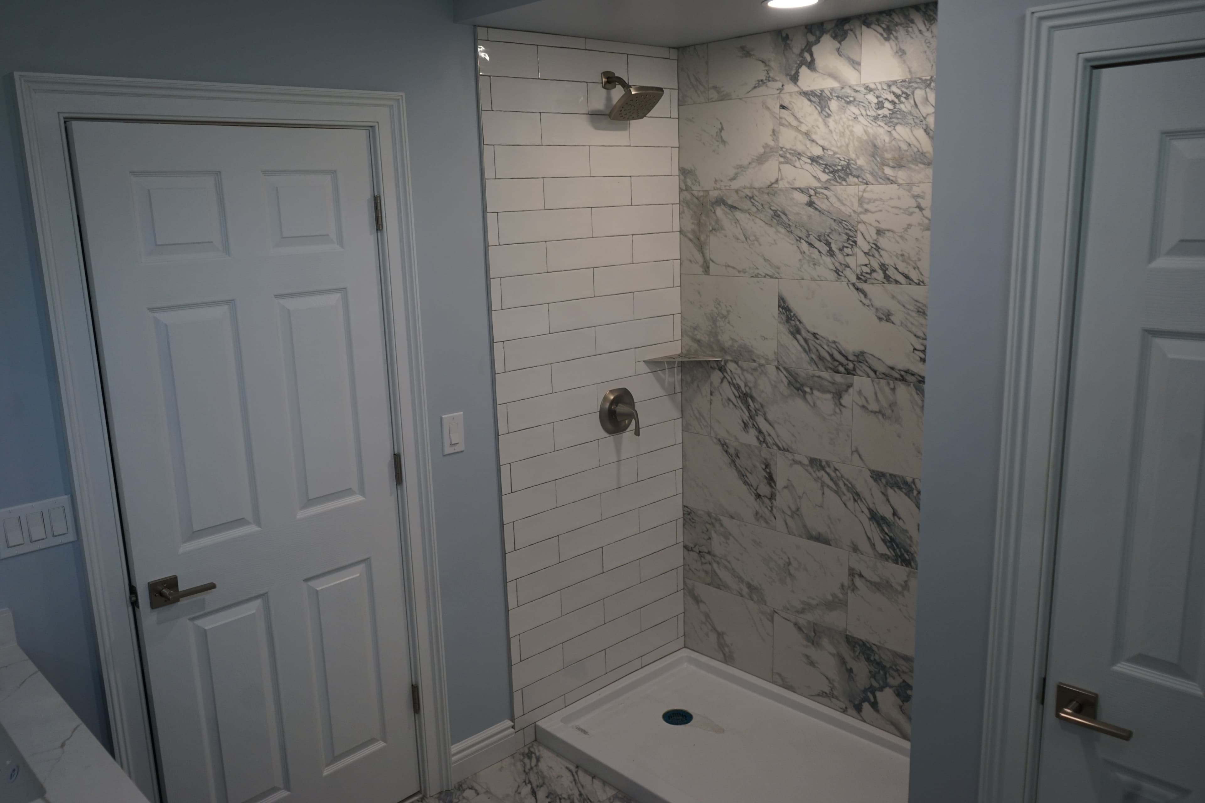 Modern bathroom with white subway tile shower, marble accent wall, and sleek fixtures.