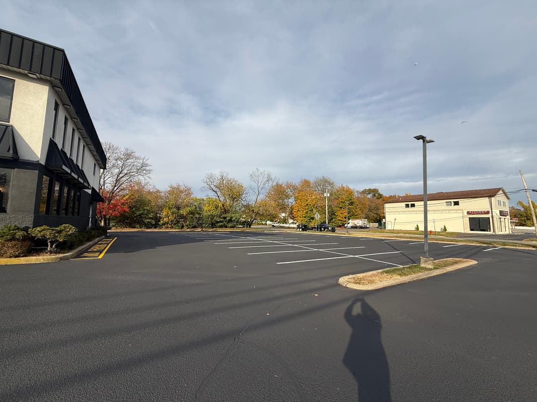 Empty parking lot with autumn trees in the background and a cloudy sky overhead.