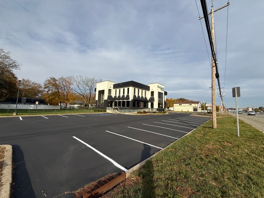 Modern commercial building with spacious parking lot and clear blue sky in the background.