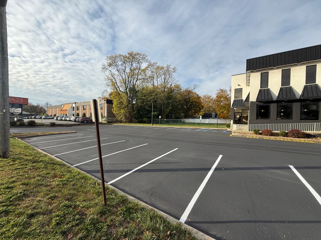 Vacant parking lot beside a commercial building under a cloudy sky. Fall foliage in background.