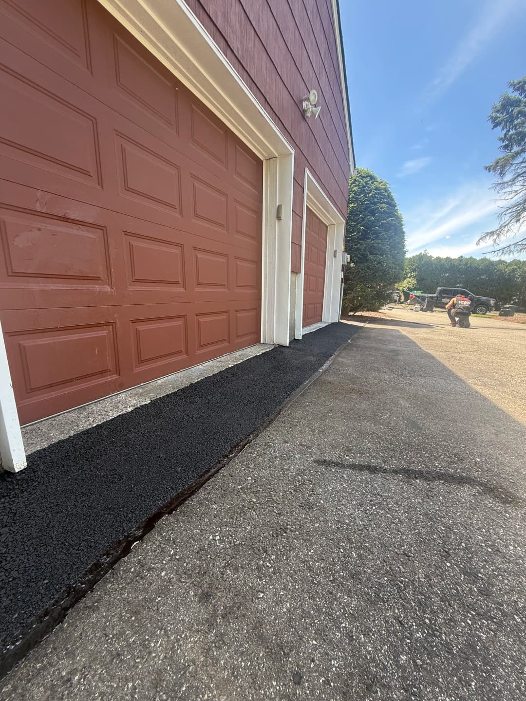 Freshly paved asphalt edging alongside red garage doors on a sunny day.