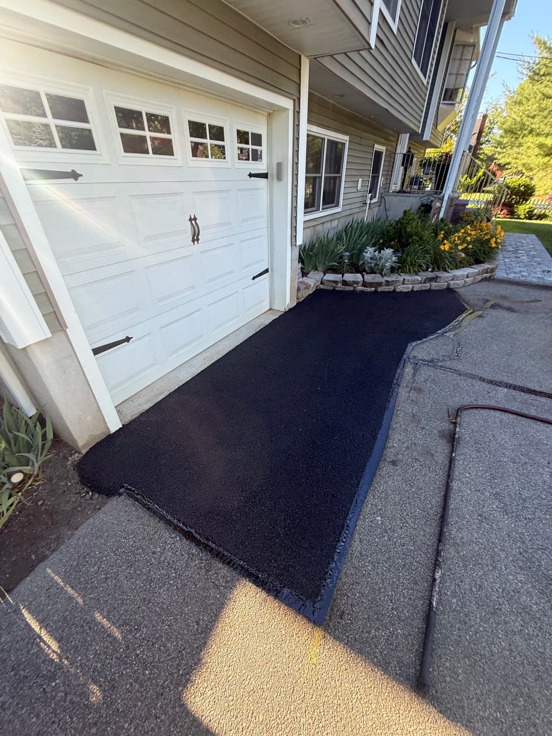 Freshly paved asphalt walkway leading to a garage with surrounding garden landscaping.