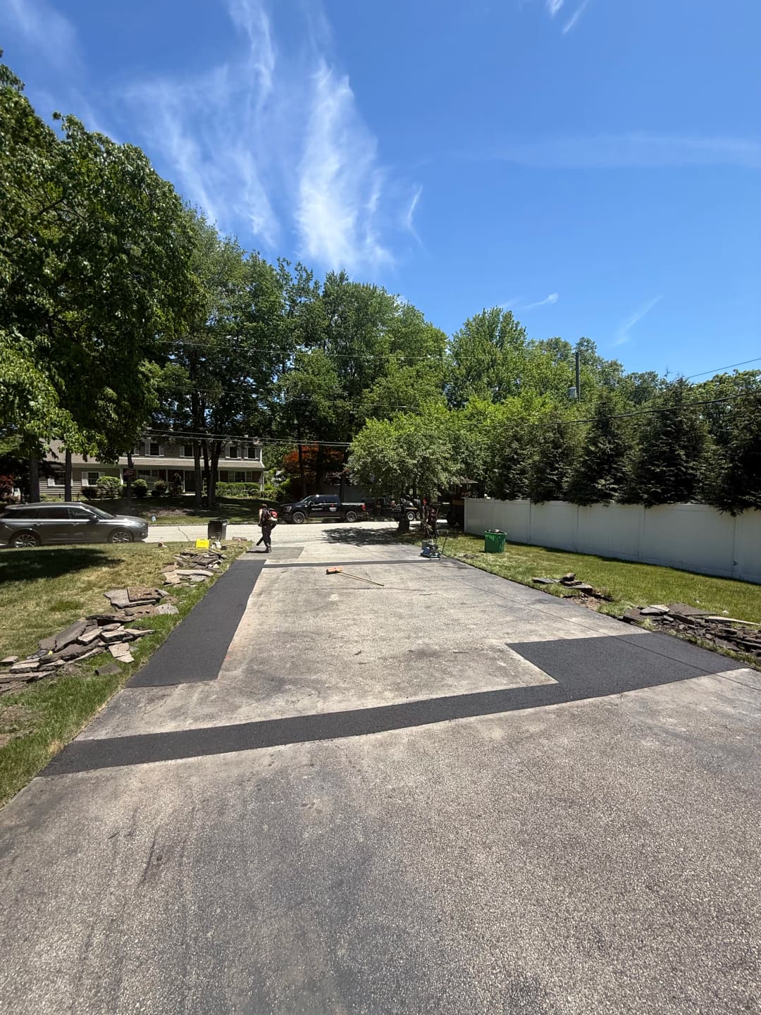 Newly asphalted driveway renovation with workers and lush green trees in the background.
