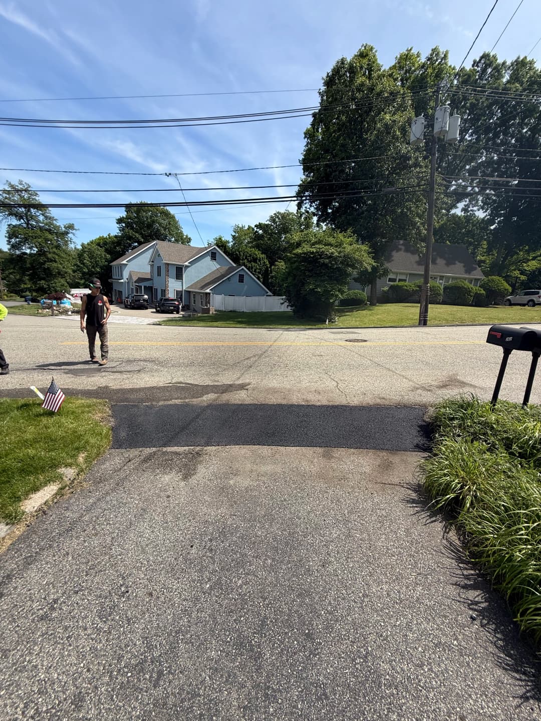 Street view with a mailbox and American flag, showcasing residential homes and clear sky.