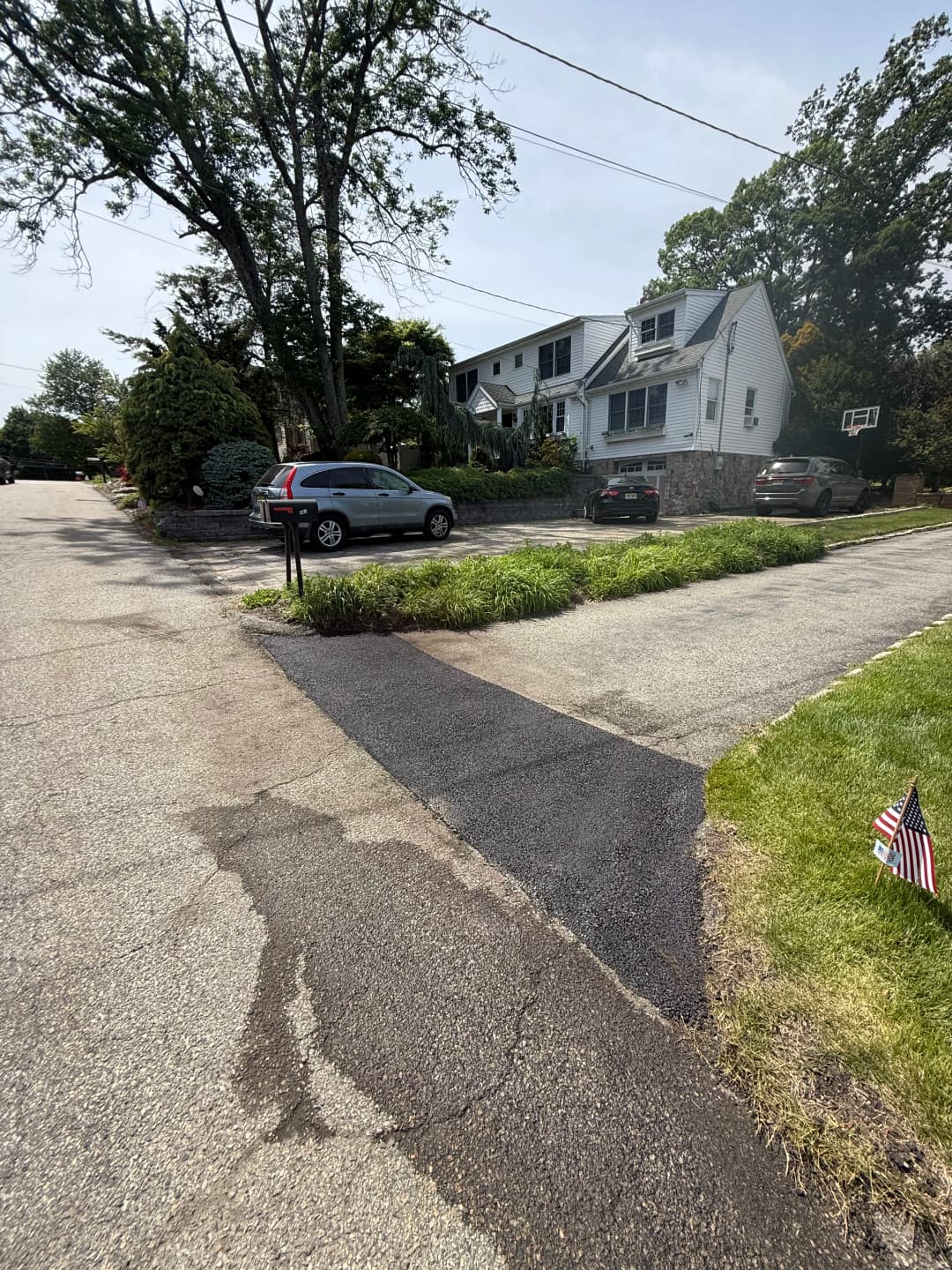 Residential street view featuring a home, front yard, and parked cars on a sunny day.