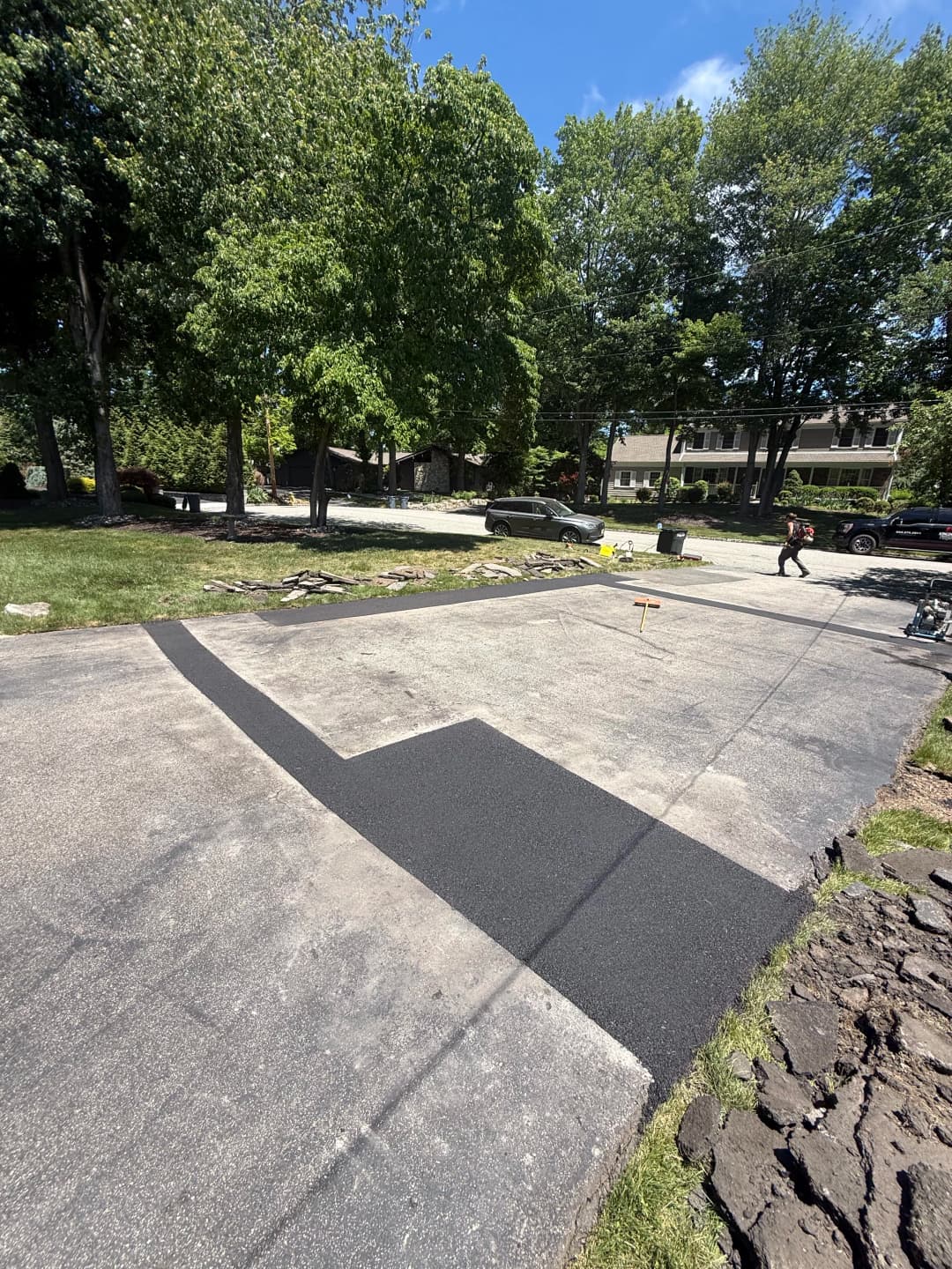 Freshly applied asphalt patch on a driveway, with trees and a house in the background.