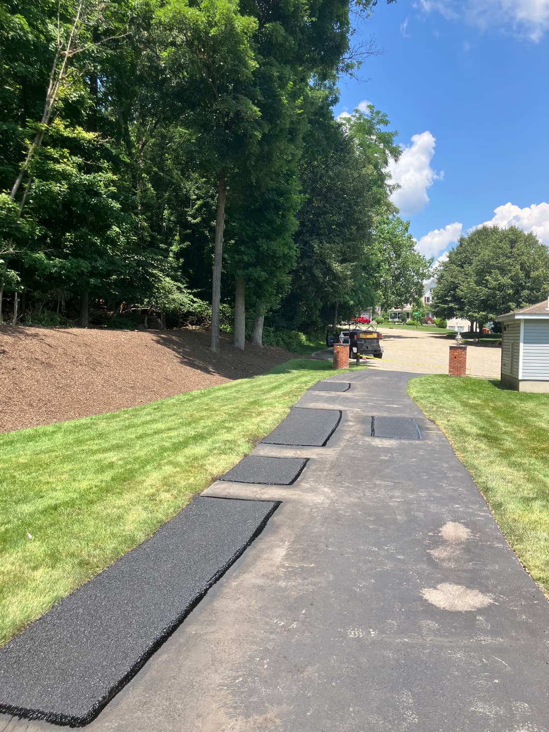 Pathway installation with freshly laid asphalt and landscaping in a residential area.