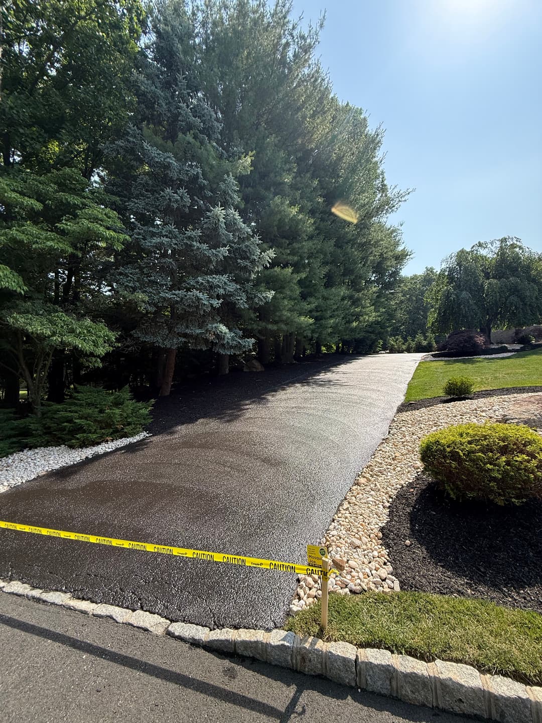 Newly paved driveway lined with decorative stones and surrounded by greenery.