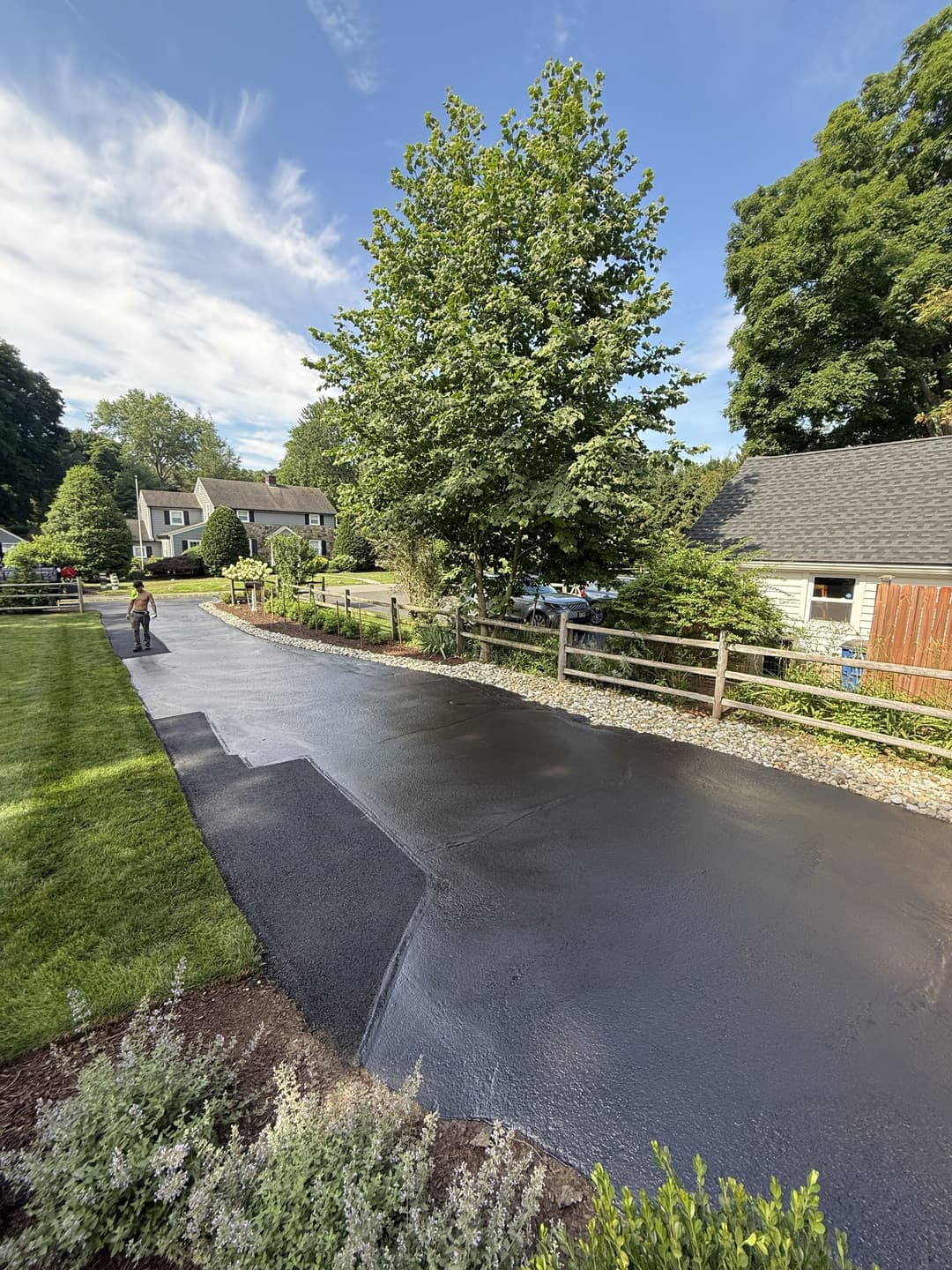 Freshly asphalted driveway installation in a residential area with green landscaping.