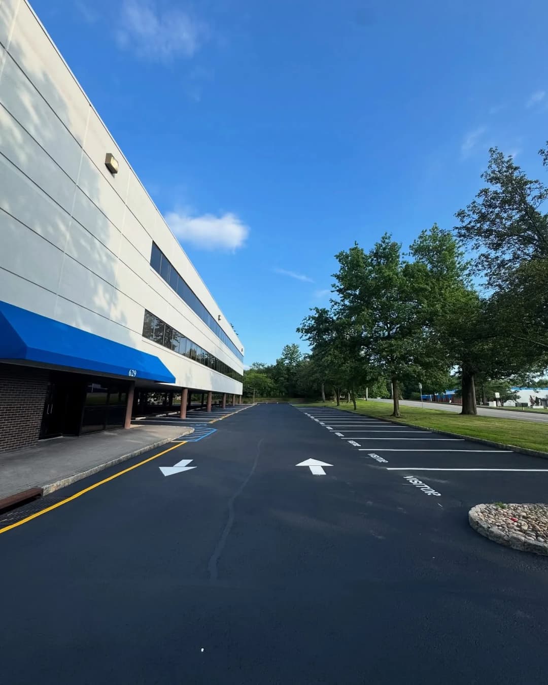 Wide view of a commercial building with blue awnings, surrounded by trees and a clear sky.