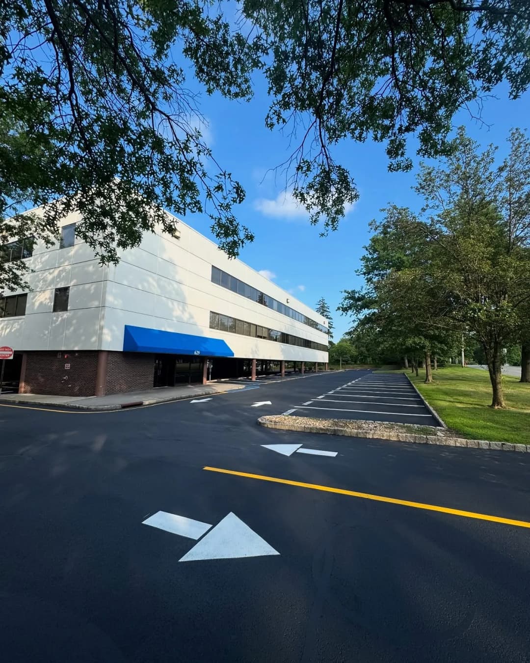 Modern office building with blue awning, fresh asphalt parking lot, and green trees.