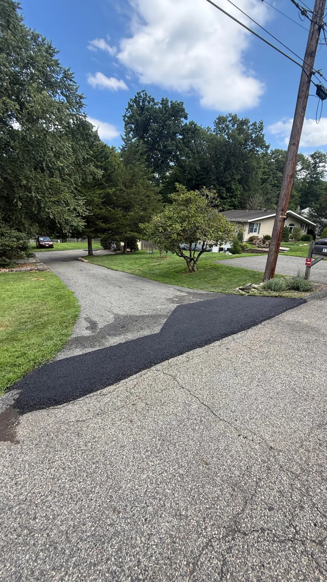 Freshly paved asphalt driveway merging with a gravel road under a clear blue sky.