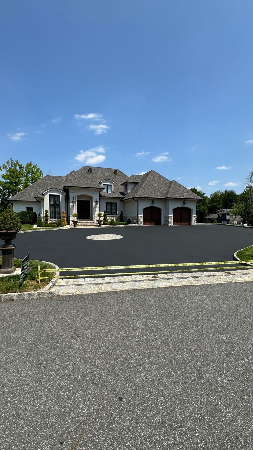 Luxury mansion with a circular driveway and manicured landscaping under a clear blue sky.