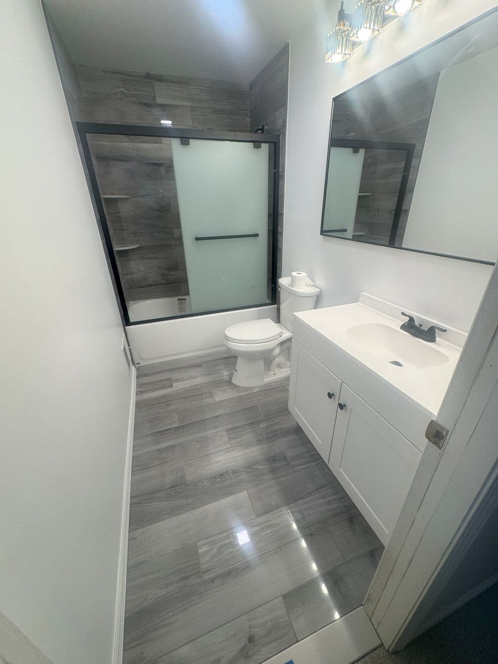 Modern bathroom with gray wood-style flooring, glass shower enclosure, and sleek vanity.