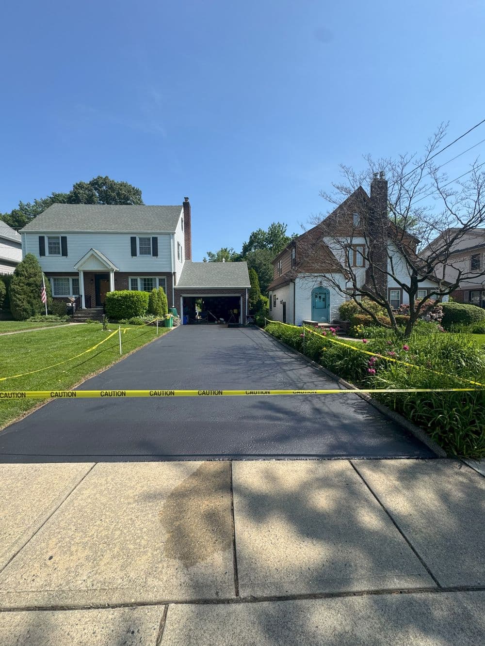 Residential driveway with caution tape in front of two homes on a sunny day.