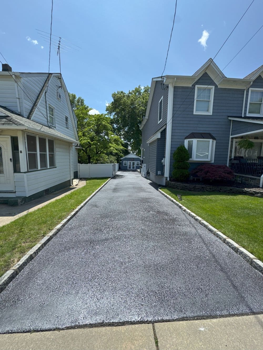 Freshly paved driveway between residential houses on a sunny day with clear blue sky.