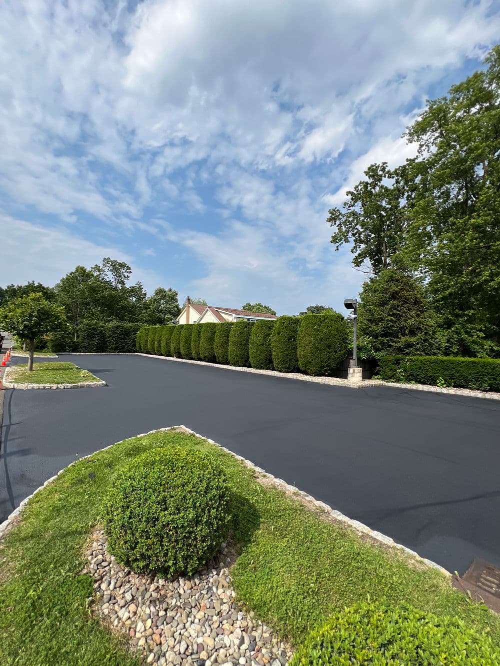 Freshly paved residential street lined with neatly trimmed hedges and decorative stone landscaping.