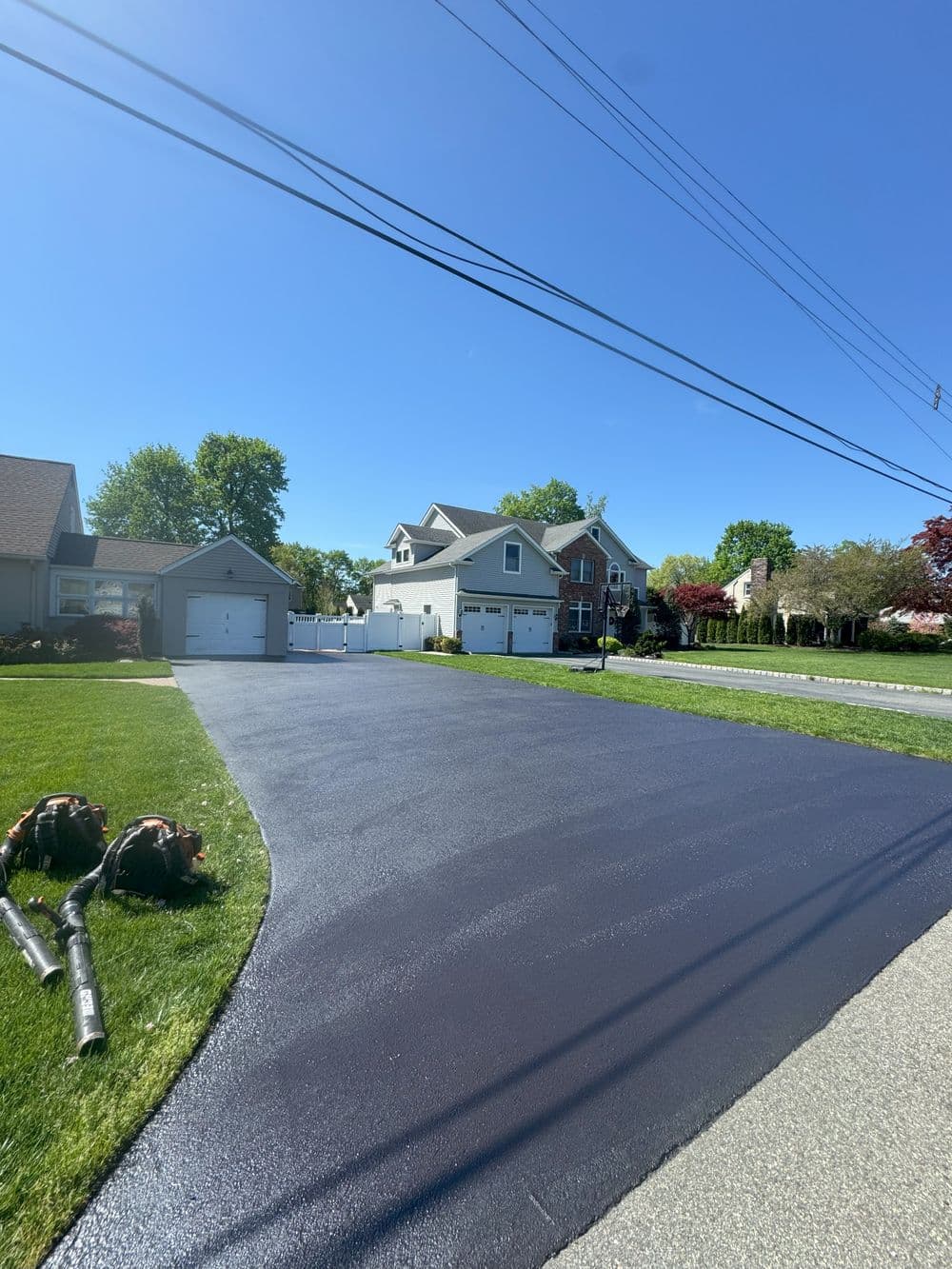 Freshly paved driveway in a suburban setting with green lawns and clear blue skies.