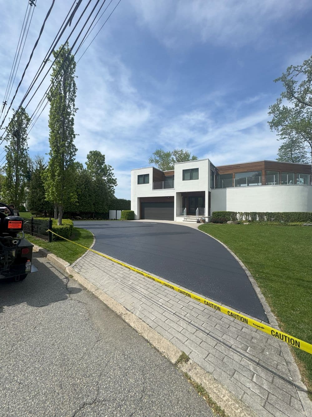 Modern house with freshly paved driveway and caution tape in front, surrounded by greenery.
