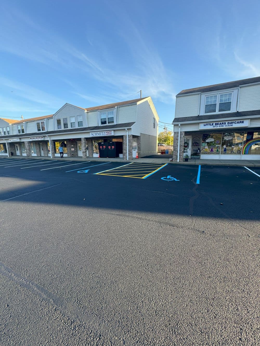 Retail storefronts with clear blue skies and parking spaces, featuring Little Bear Daycare.
