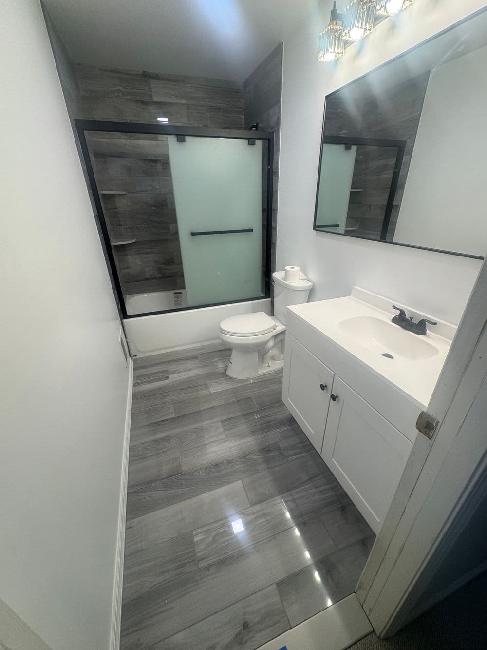 Modern bathroom with shower, vanity, and gray tile flooring, bright lighting, and mirrors.