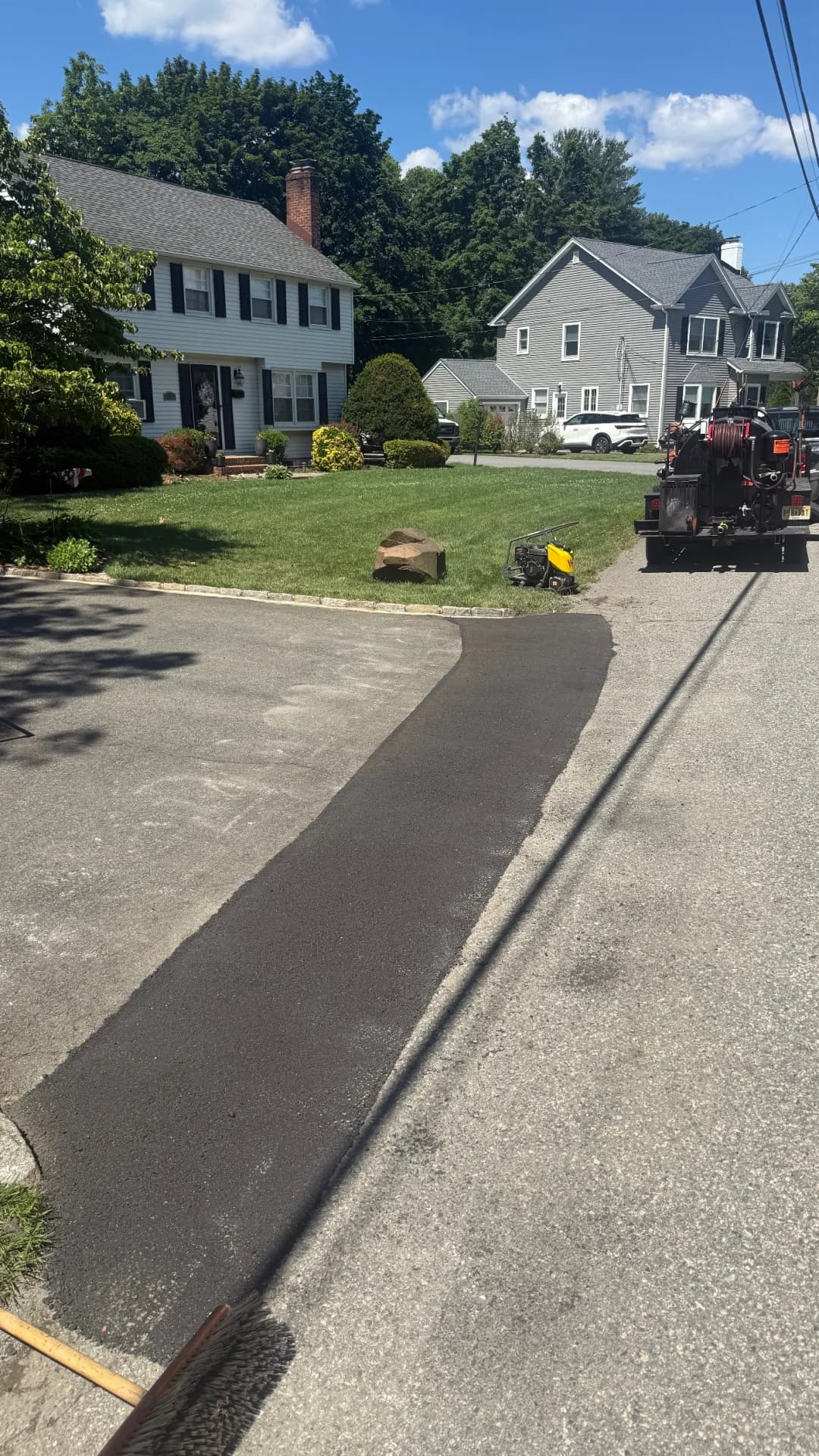 Freshly paved asphalt driveway in a residential area with homes and green landscape.
