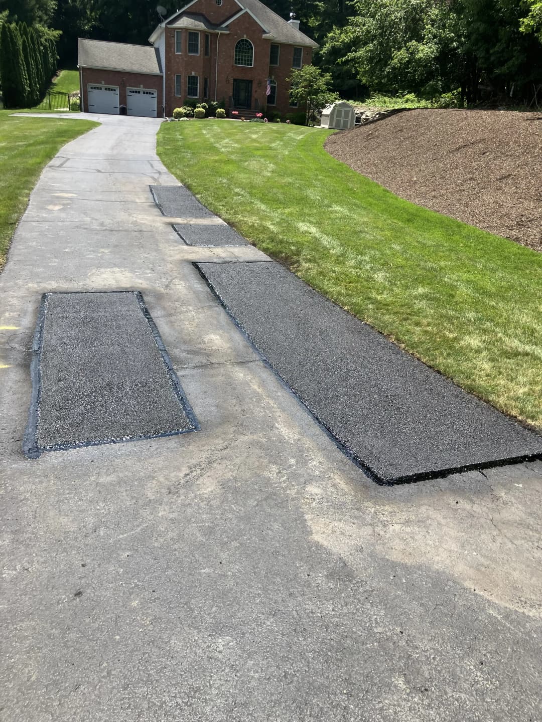 Freshly paved sections on a residential driveway outside a brick home.