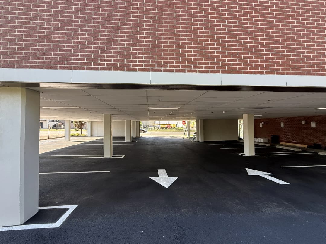 Covered parking area with brick wall and clear directional arrows on asphalt.