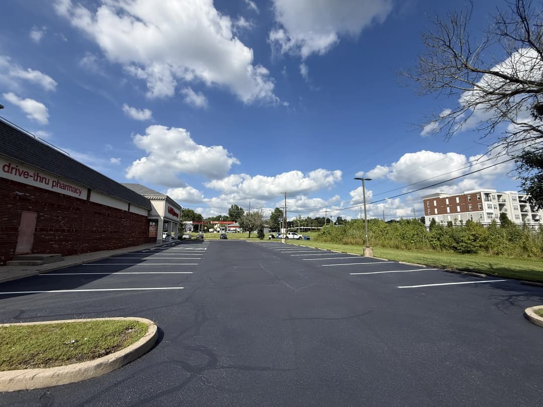 Empty parking lot of a drive-thru pharmacy under a blue sky with scattered clouds.