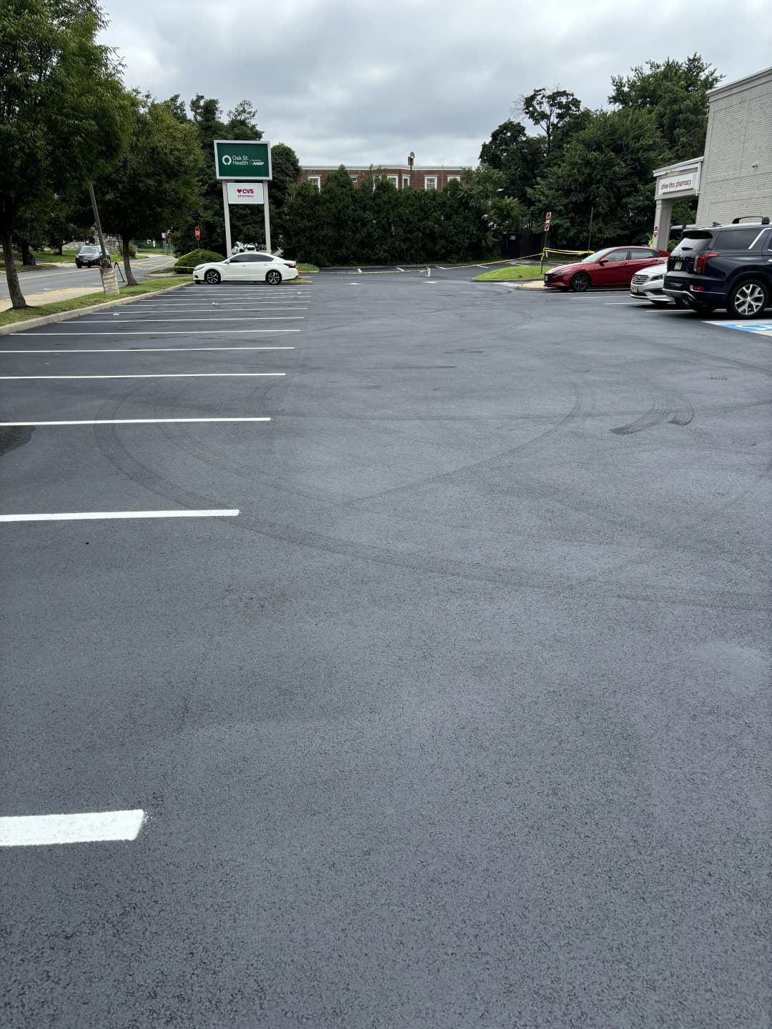 Empty parking lot with clear lines, trees in background, and nearby storefronts.
