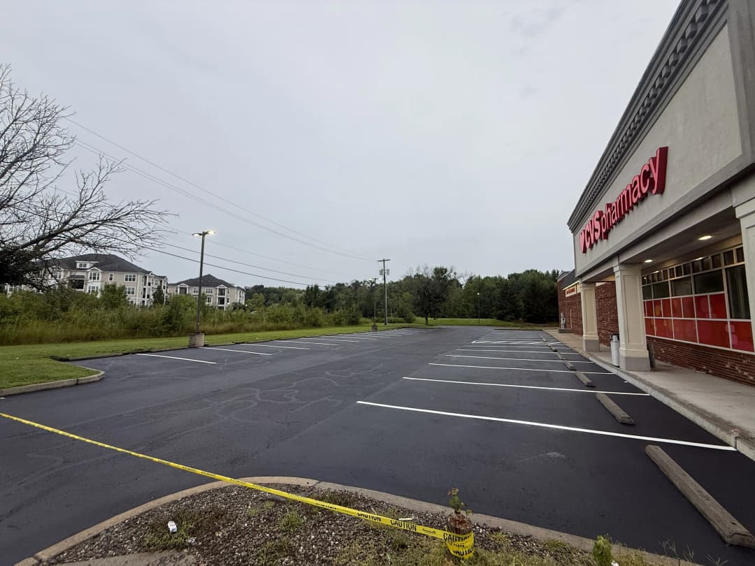 Empty parking lot beside a pharmacy with nearby residential buildings and overcast sky.