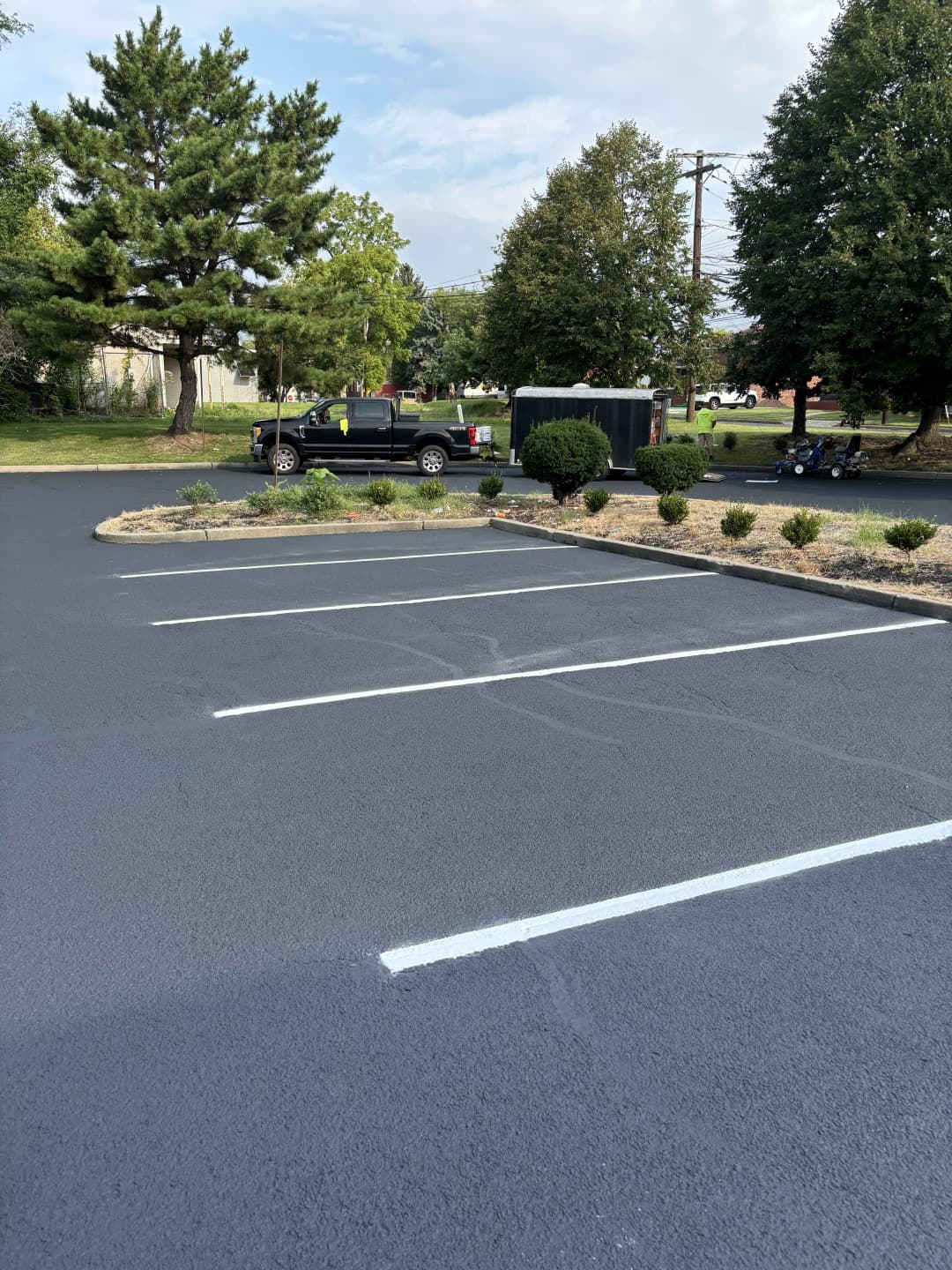 Freshly paved parking lot with white stripes, trees, and a truck in the background.
