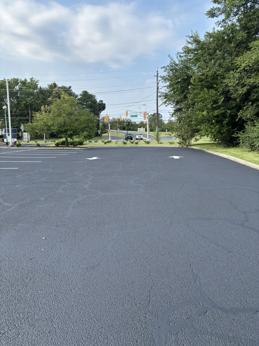 Empty asphalt parking lot with directional arrows and greenery in the background.